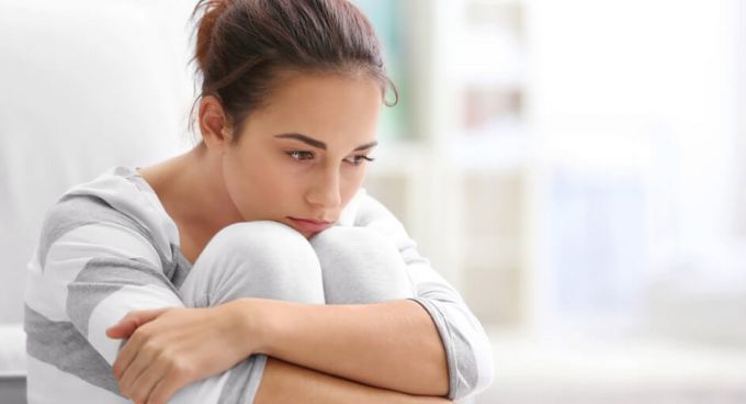 Eine junge Frau umschlingt ihre Beine und sieht traurig aus