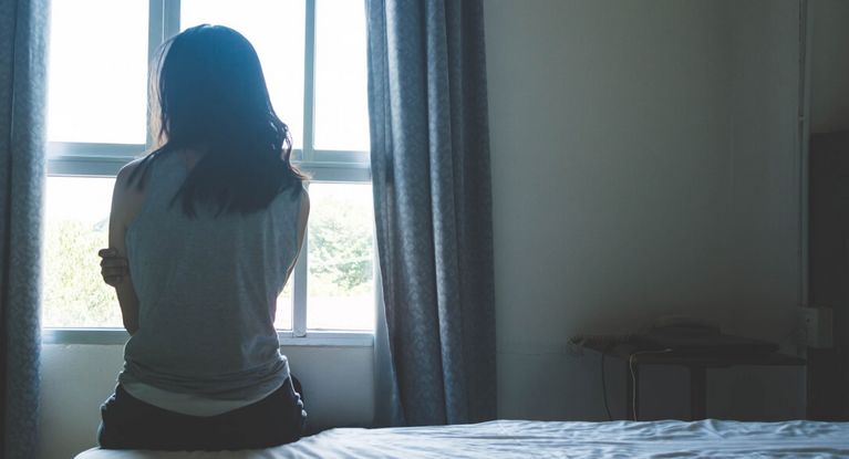 Eine Frau sitzt auf dem Bett und schaut nachdenklich aus dem Fenster