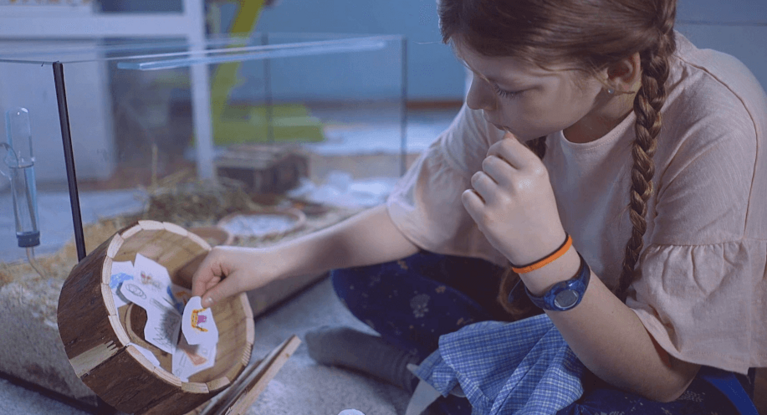 Mädchen sitzt vor Hamsterkäfig